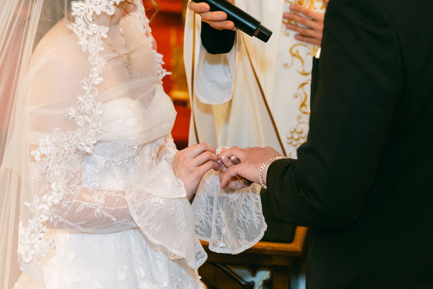 Bride and groom exchanging rings during a church wedding ceremony, bride wearing lace gown and veil.