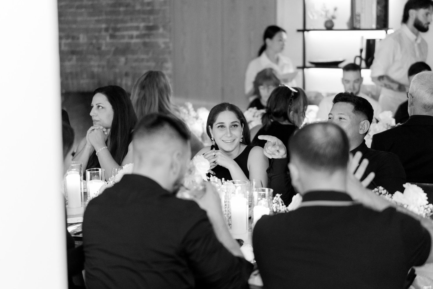 Black and white photo of guests dining and socializing at an elegant wedding reception.
