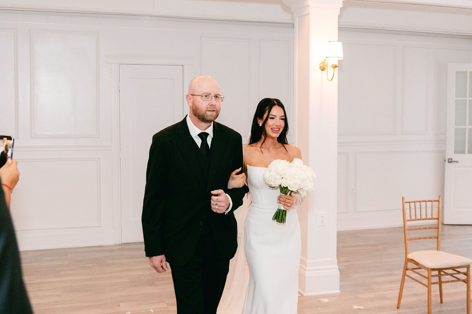 Wedding attendees in formal attire embrace during an elegant indoor ceremony.