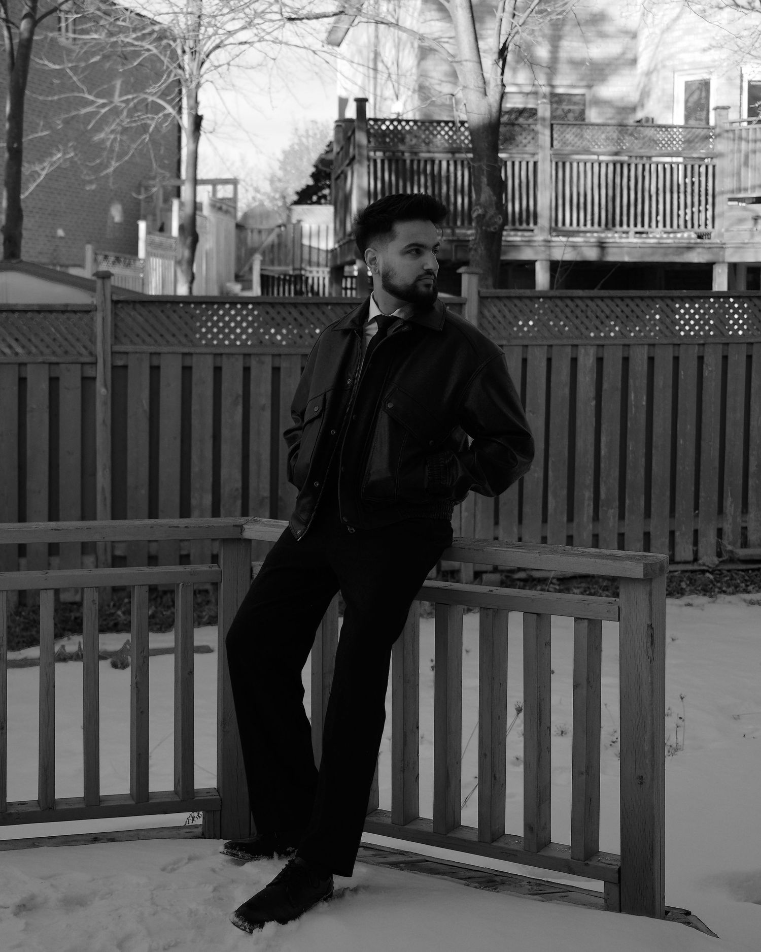 A stylishly dressed person poses by a wooden fence in a black and white photograph.