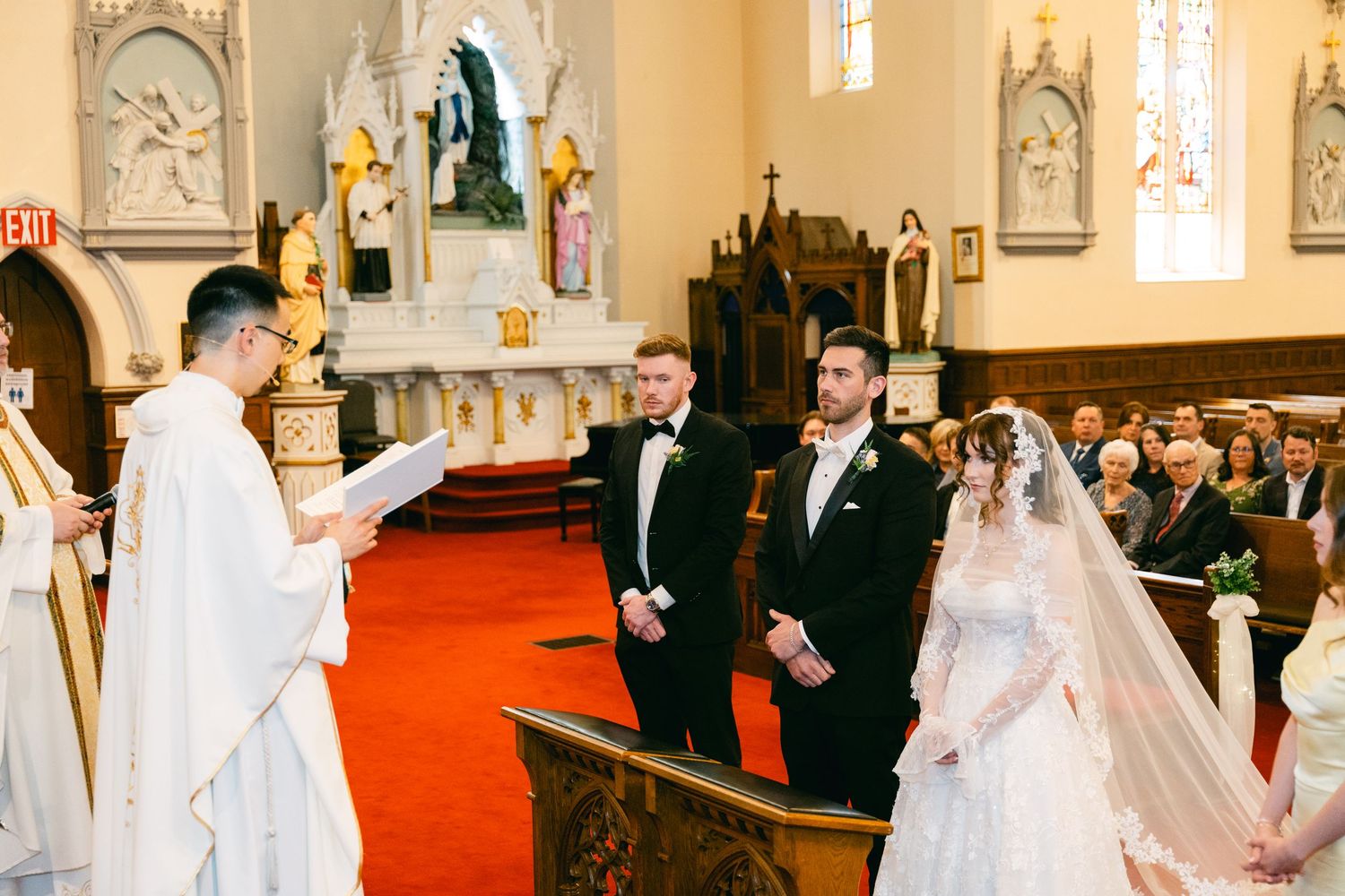 Bride and groom stand at the altar during a traditional Catholic church wedding ceremony with guests seated in pews.