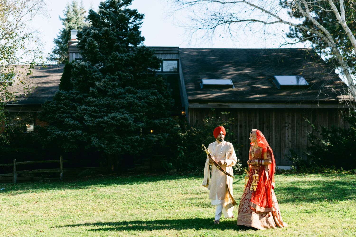 Bride in red dress and groom in light suit walking together outside rustic building.
