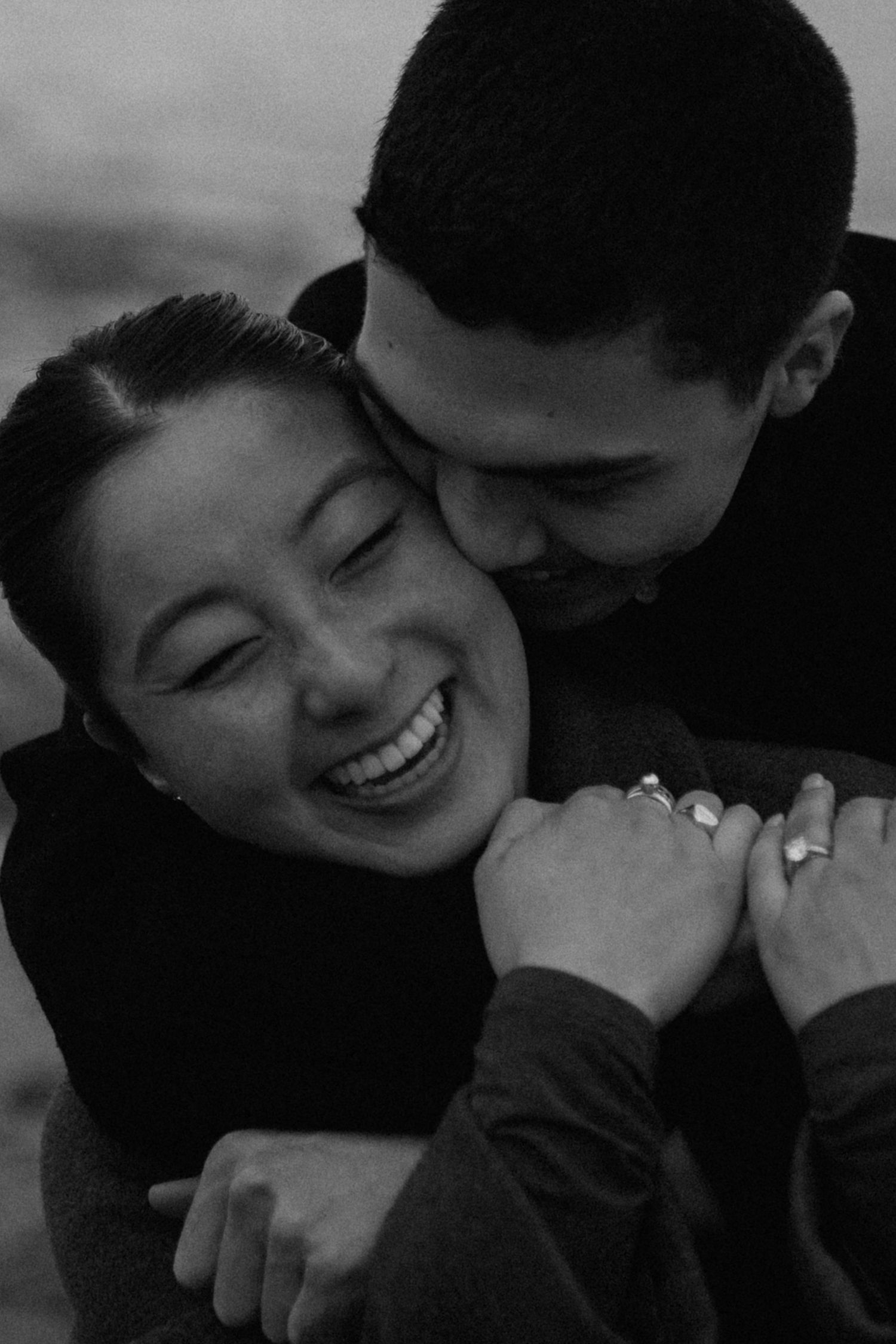 Laughing couple holding each other close after a proposal. Photographed with a black and white film style in Vancouver, BC.