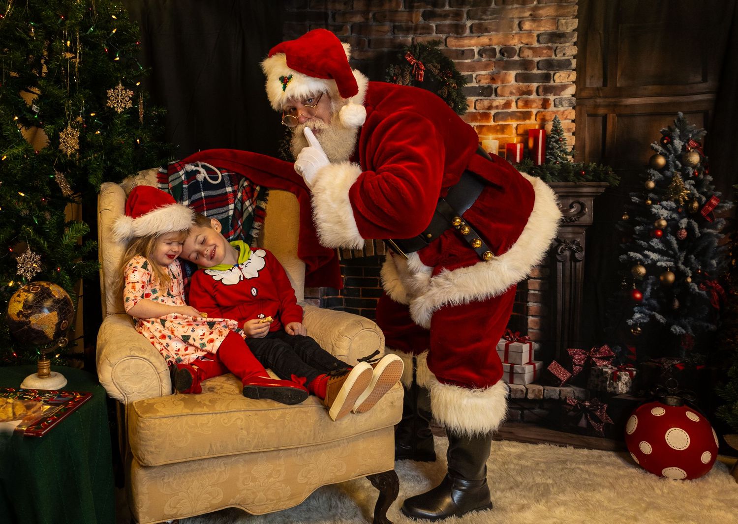 A festive Christmas scene shows someone in a traditional red Santa suit arranging presents by a decorated tree and fireplace.