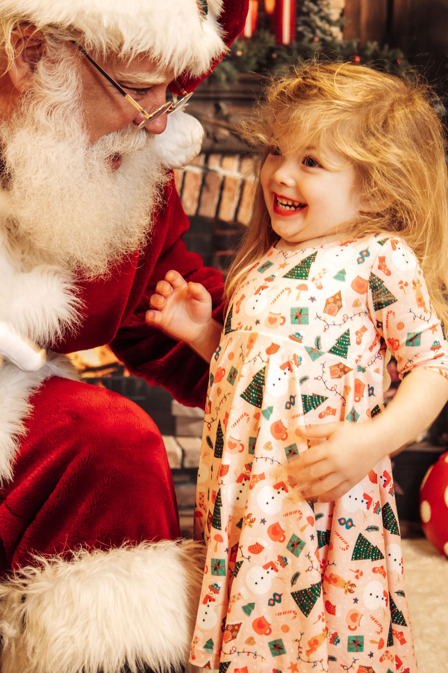 A child in festive Christmas pajamas shares a joyful moment with Santa Claus during a holiday photo session.