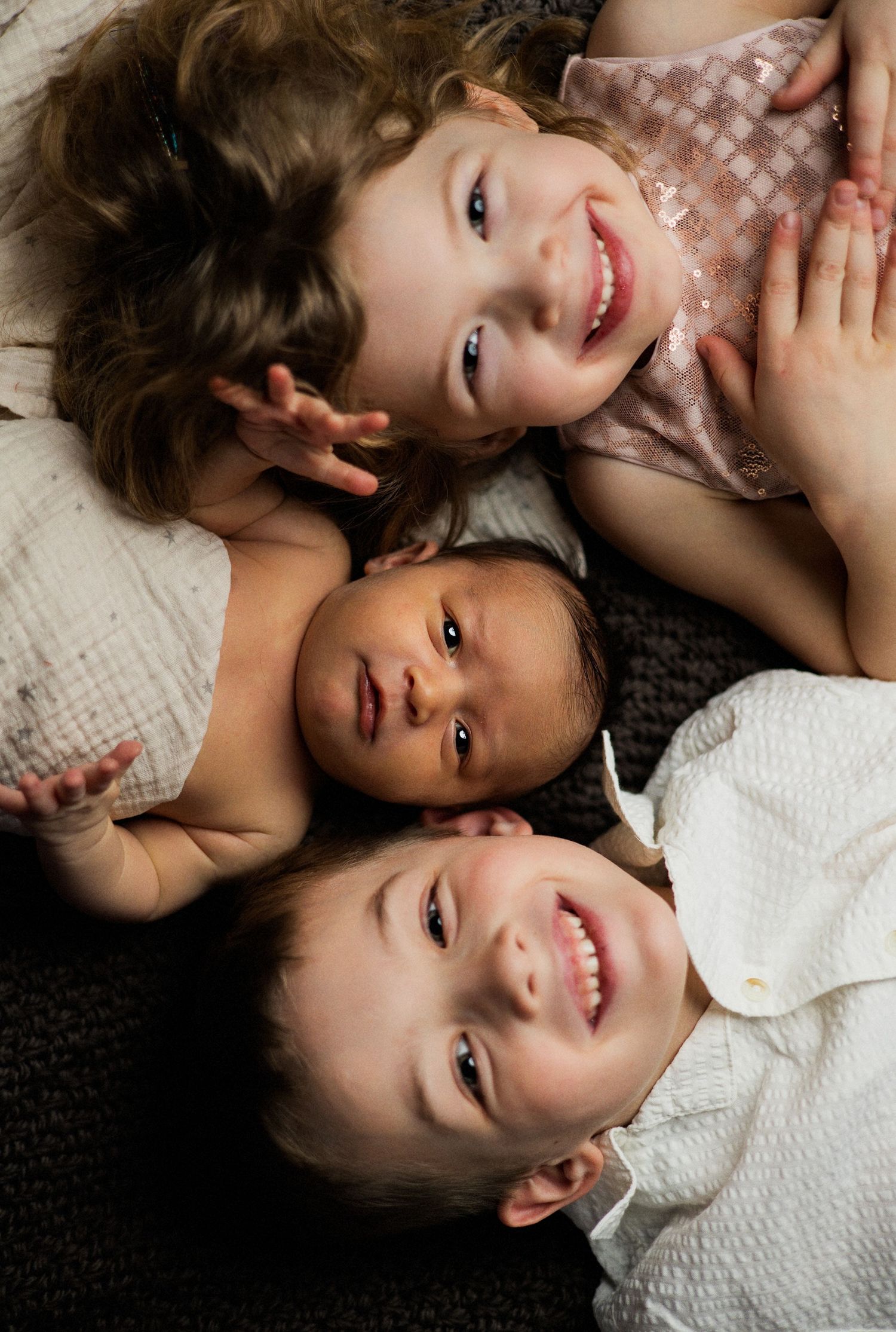Two children lying on a light colored blanket or carpet while smiling and playing together.