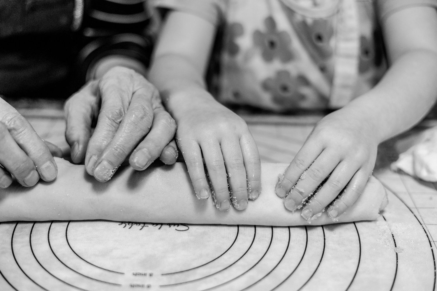 Black and white photo showing hands kneading and rolling dough on a floured surface with circular patterns.
