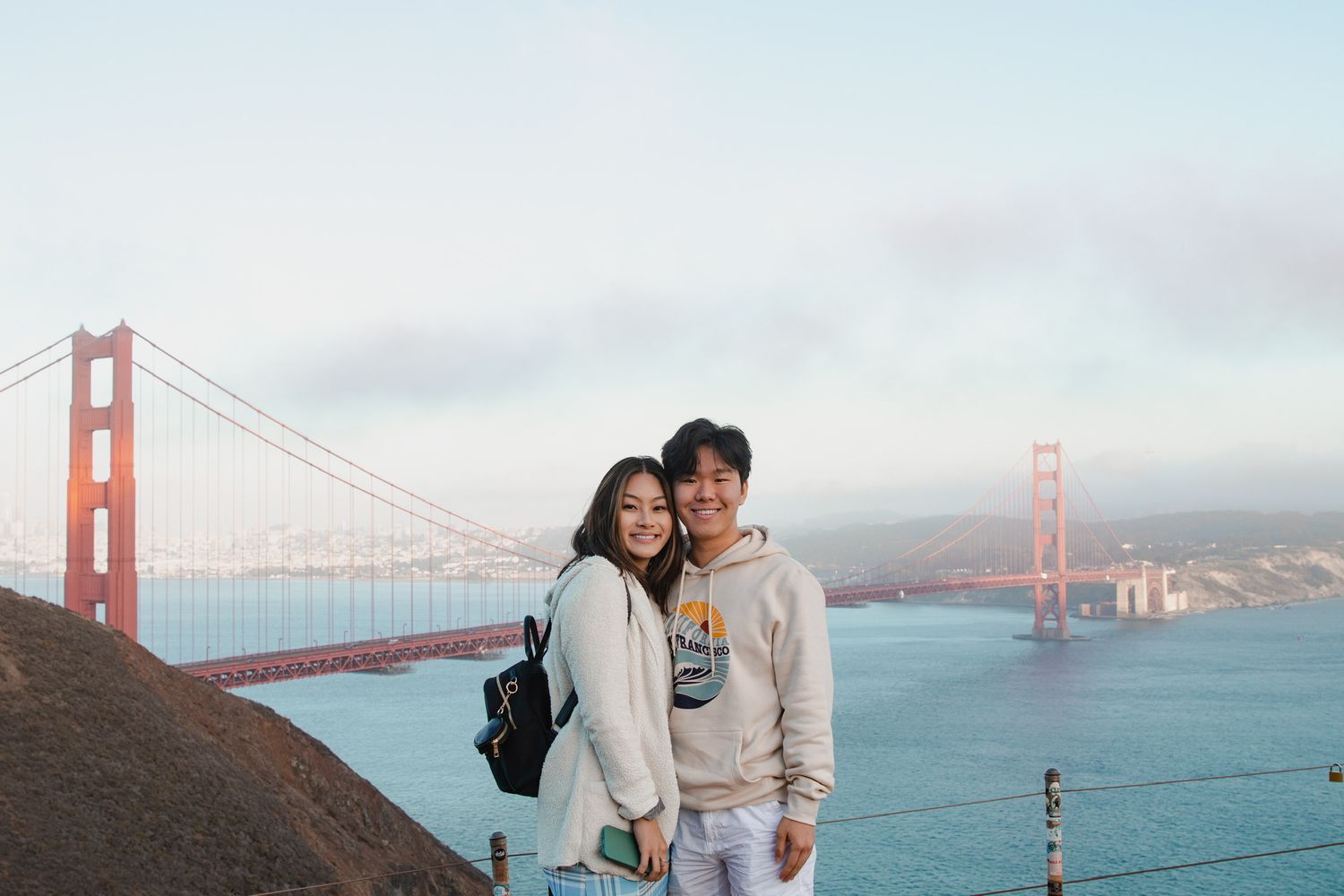 A couple poses together with the iconic Golden Gate Bridge and San Francisco Bay in the background.