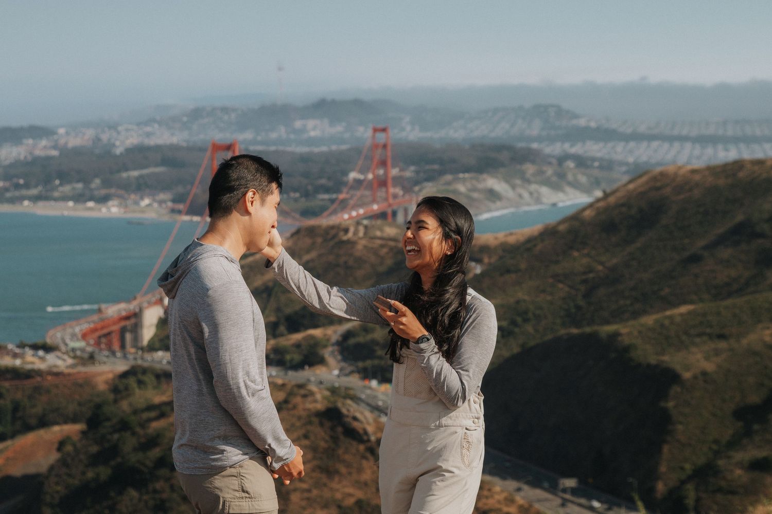 A couple shares an intimate moment overlooking the San Francisco Bay and Golden Gate Bridge on a misty afternoon.