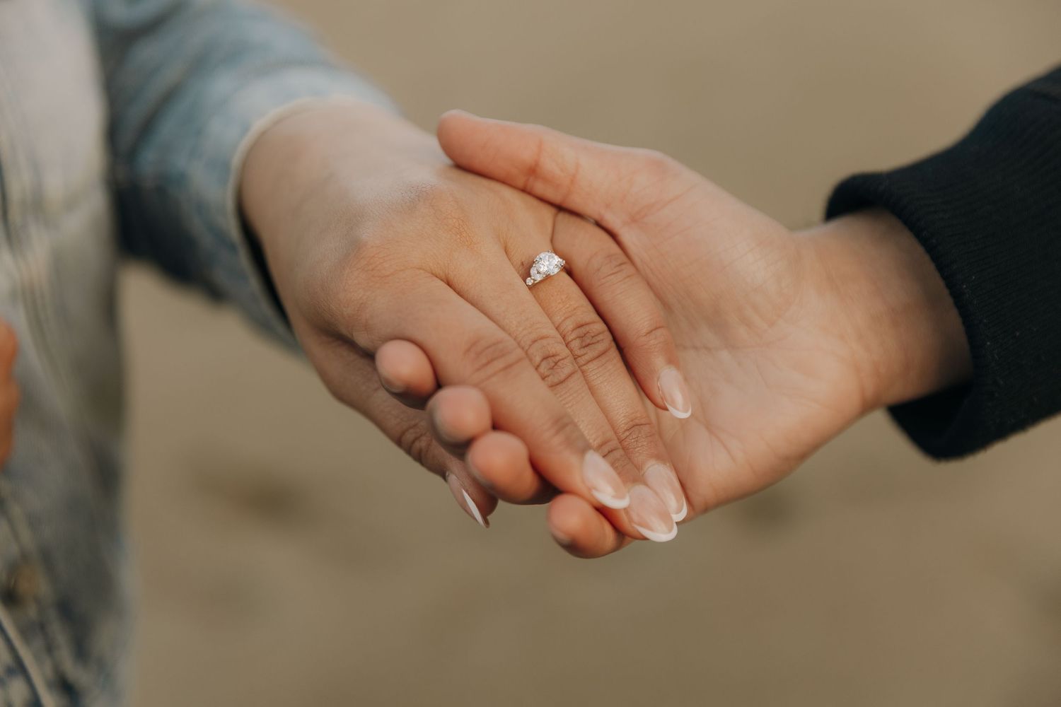 Close-up shot of two hands clasped together, with an engagement ring visible on one hand.