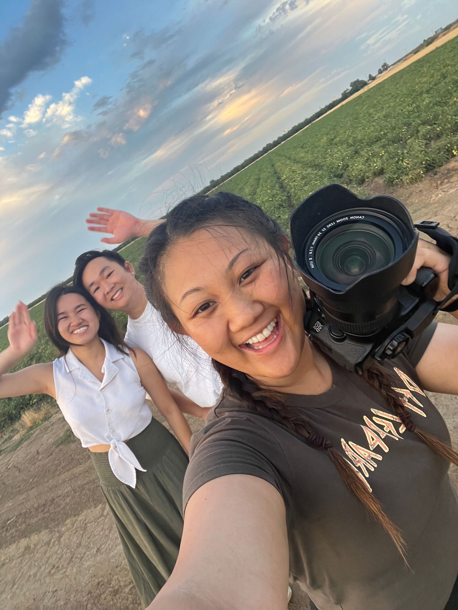 Photographer taking group selfie in open field during golden hour sunset.