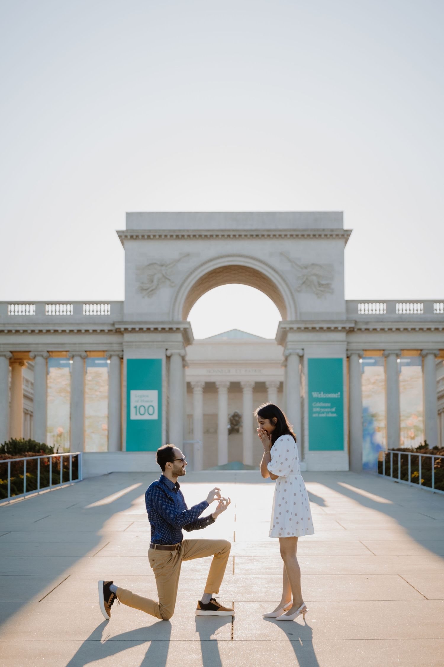 A romantic marriage proposal moment captured at Legion of Honor museum in San Francisco with classical architecture.