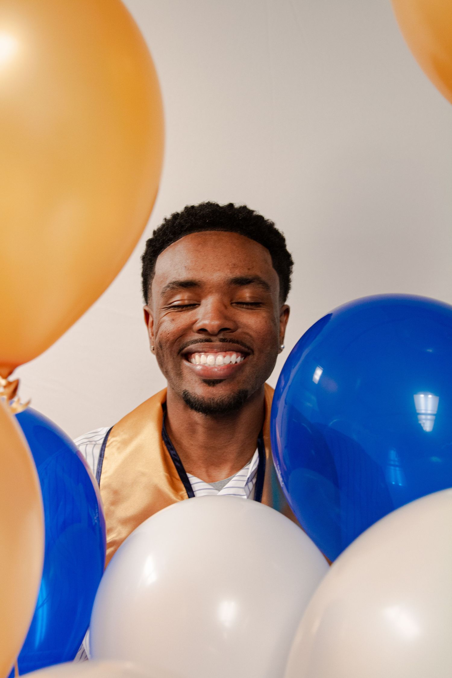 Graduate in gold stole poses with blue and white balloons during celebration.