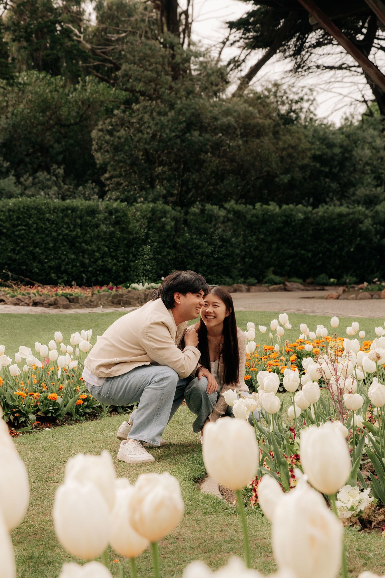 Couple crouching together in a blooming tulip garden with white flowers in foreground.