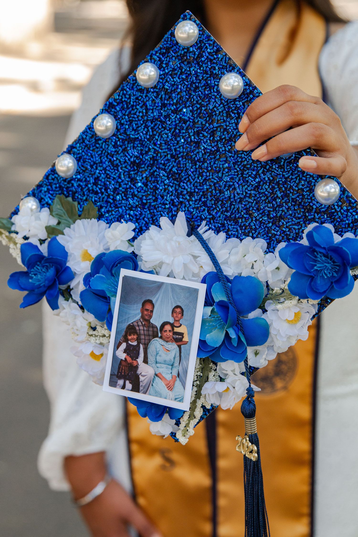 Decorated graduation cap with blue glitter, white flowers and pearls displays a family photo.