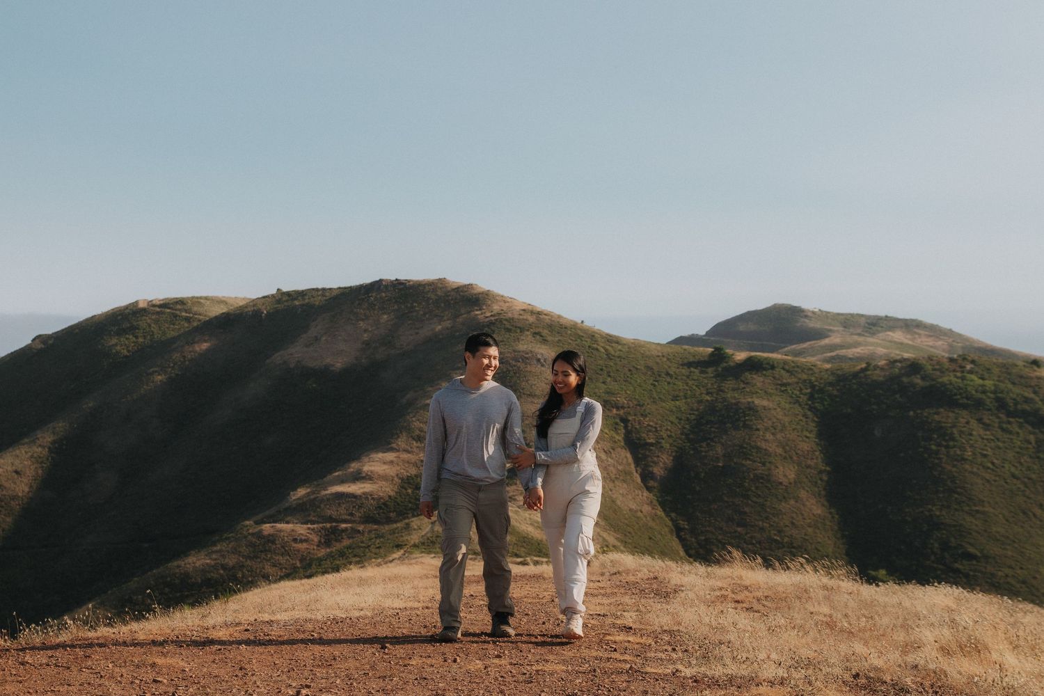 Couple walking together on a scenic mountain ridge during golden hour with rolling hills in the background.