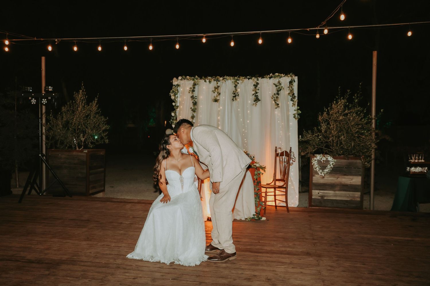 A couple shares an intimate moment under string lights during an outdoor evening wedding celebration.