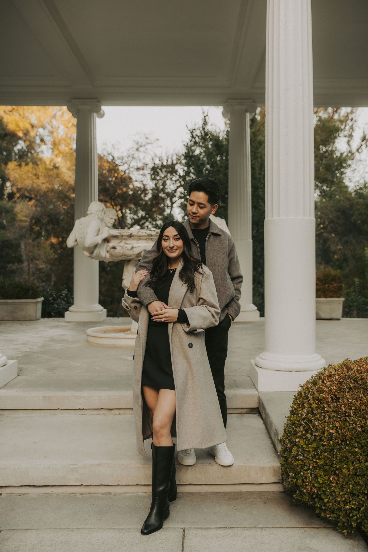 A couple shares a playful moment on a white columned porch surrounded by autumn foliage.