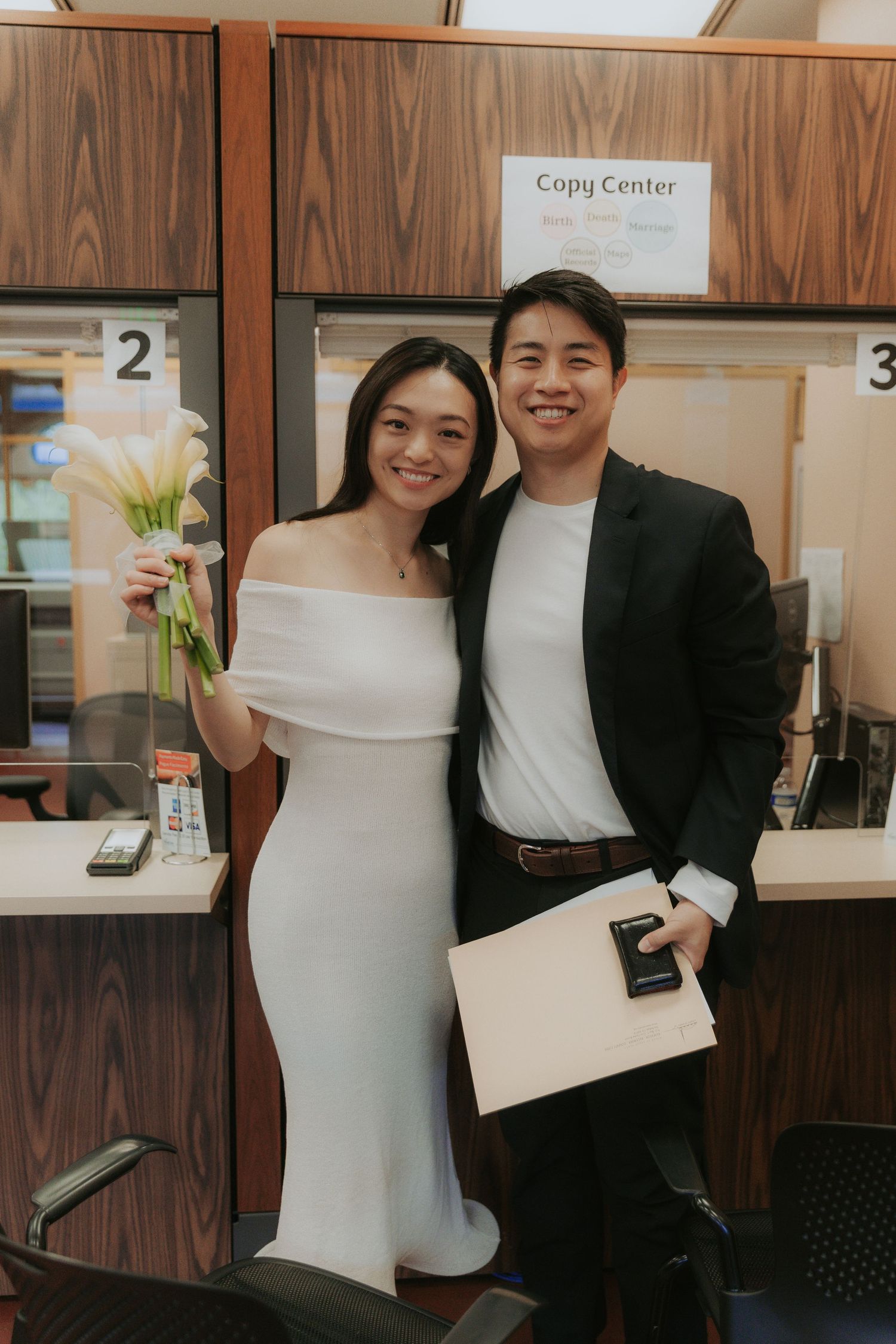 Formal couple posing together at a copy center with documents in hand.