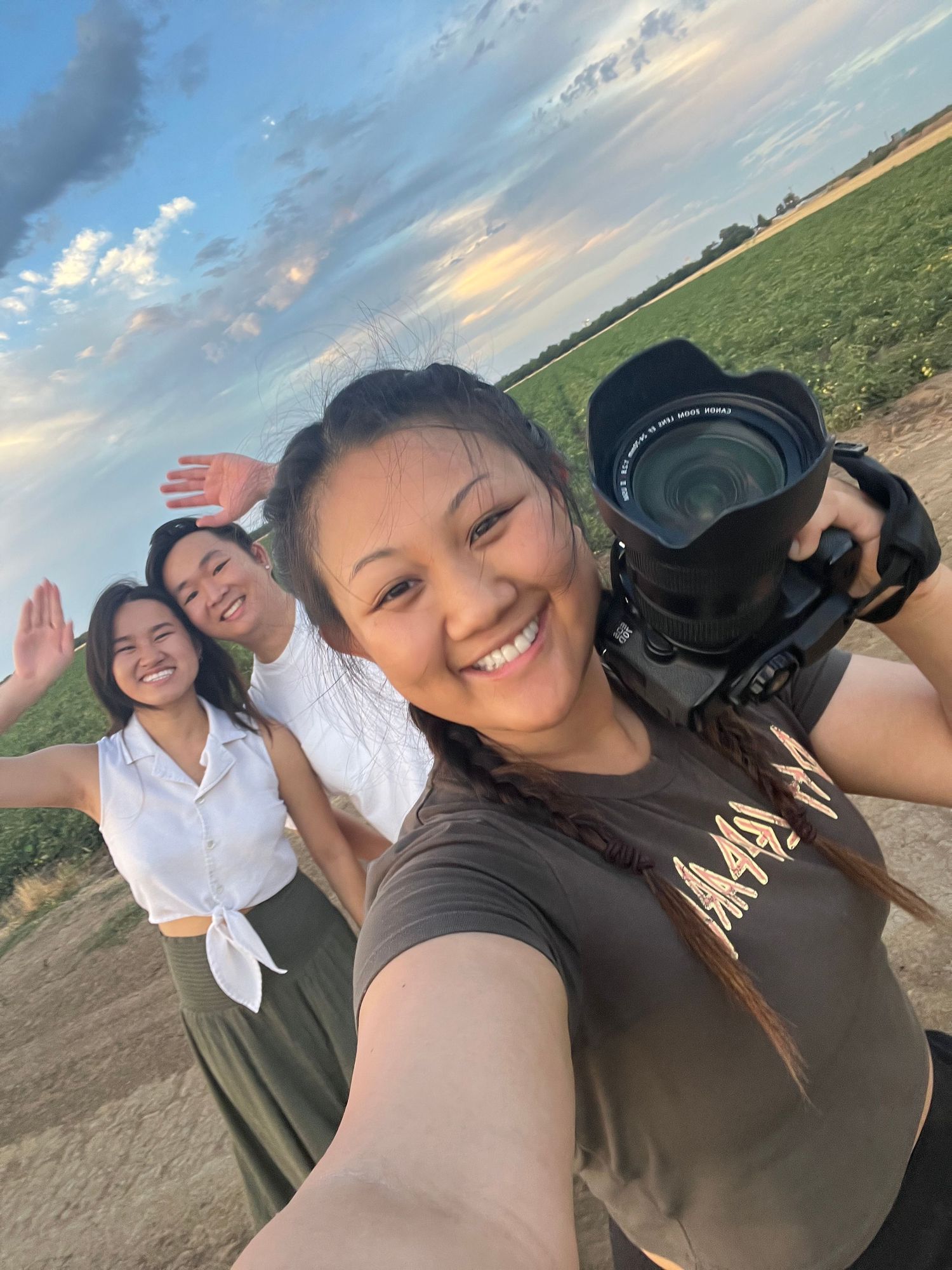 Photographer taking selfie in rural field during sunset with camera gear.