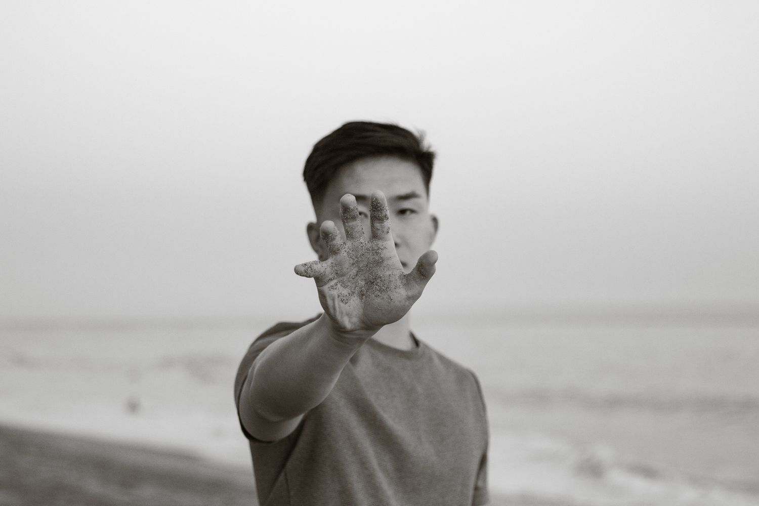 Person in a cap making a hand gesture towards the camera in black and white photography.