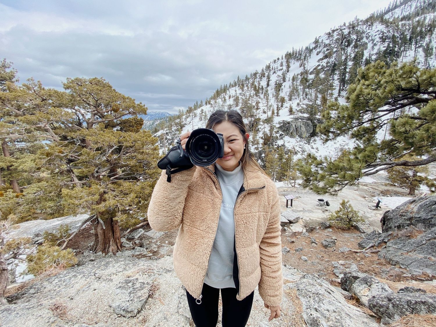 Person in beige jacket taking photos in snowy mountain landscape.