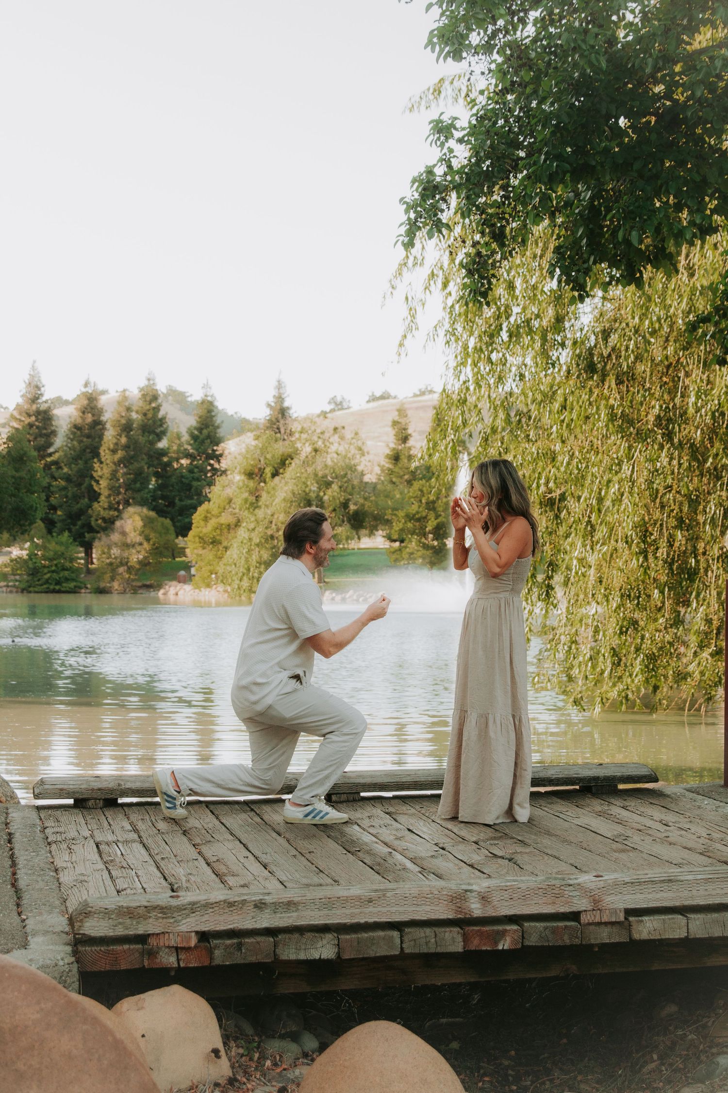 A sequence of romantic photos shows a couple sitting on a wooden dock by a tranquil lake surrounded by willow trees.