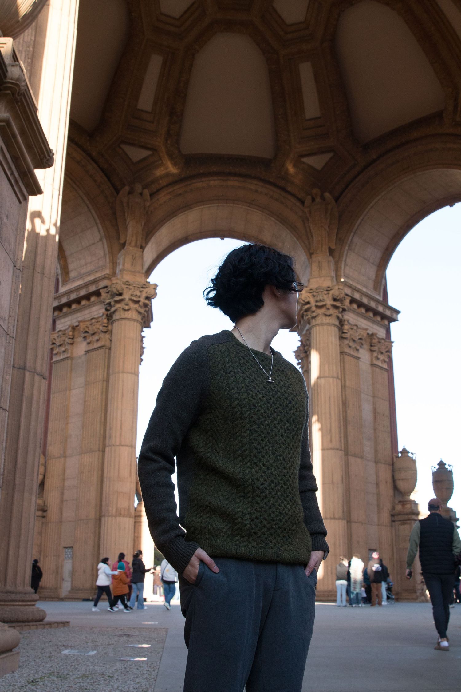 Person wearing green sweater stands beneath ornate stone archway at Palace of Fine Arts in San Francisco.