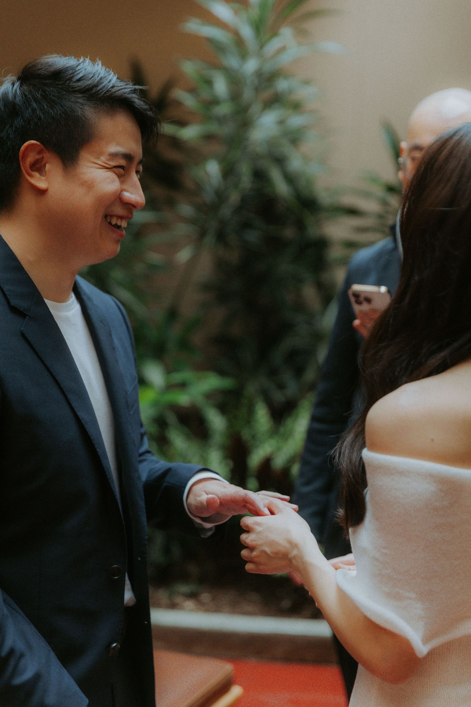 A couple in formal attire share a romantic dance moment at an indoor venue with greenery in the background.