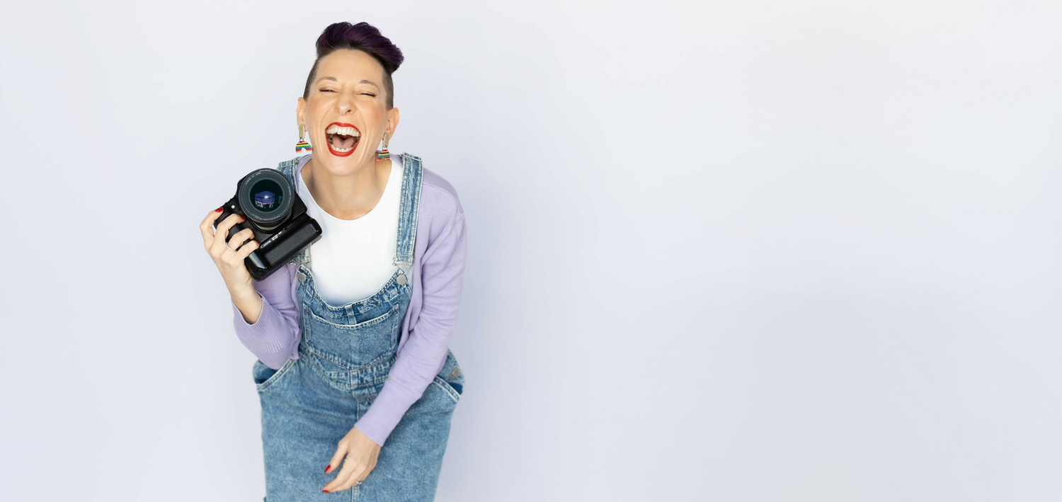 Candid portrait of photographer laughing while holding camera on white background.