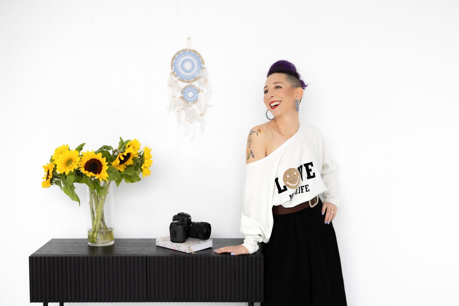 Person in white sweater standing next to black cabinet with sunflowers in vase.