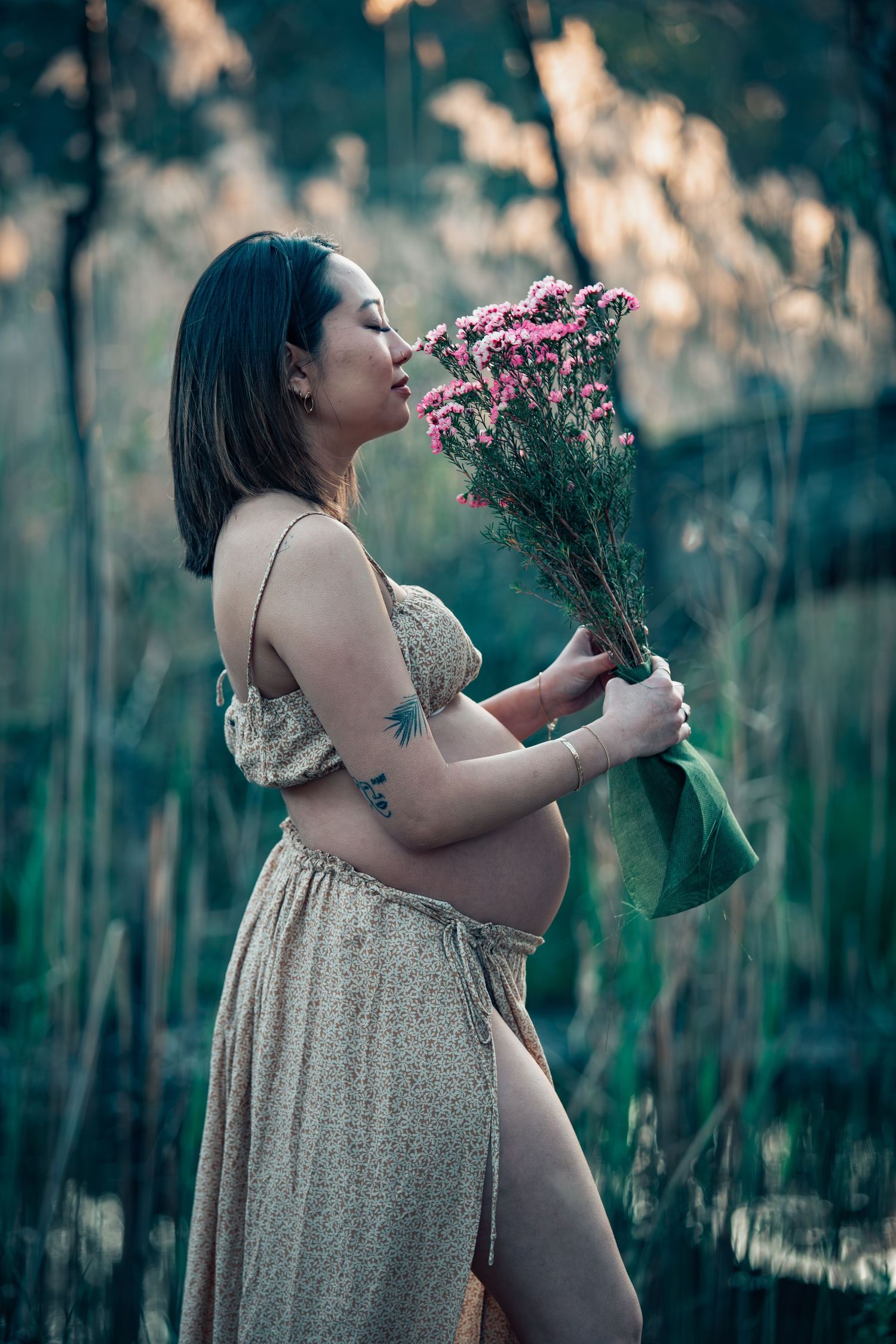 Artistic maternity photo with pink flowers in ethereal garden setting.
