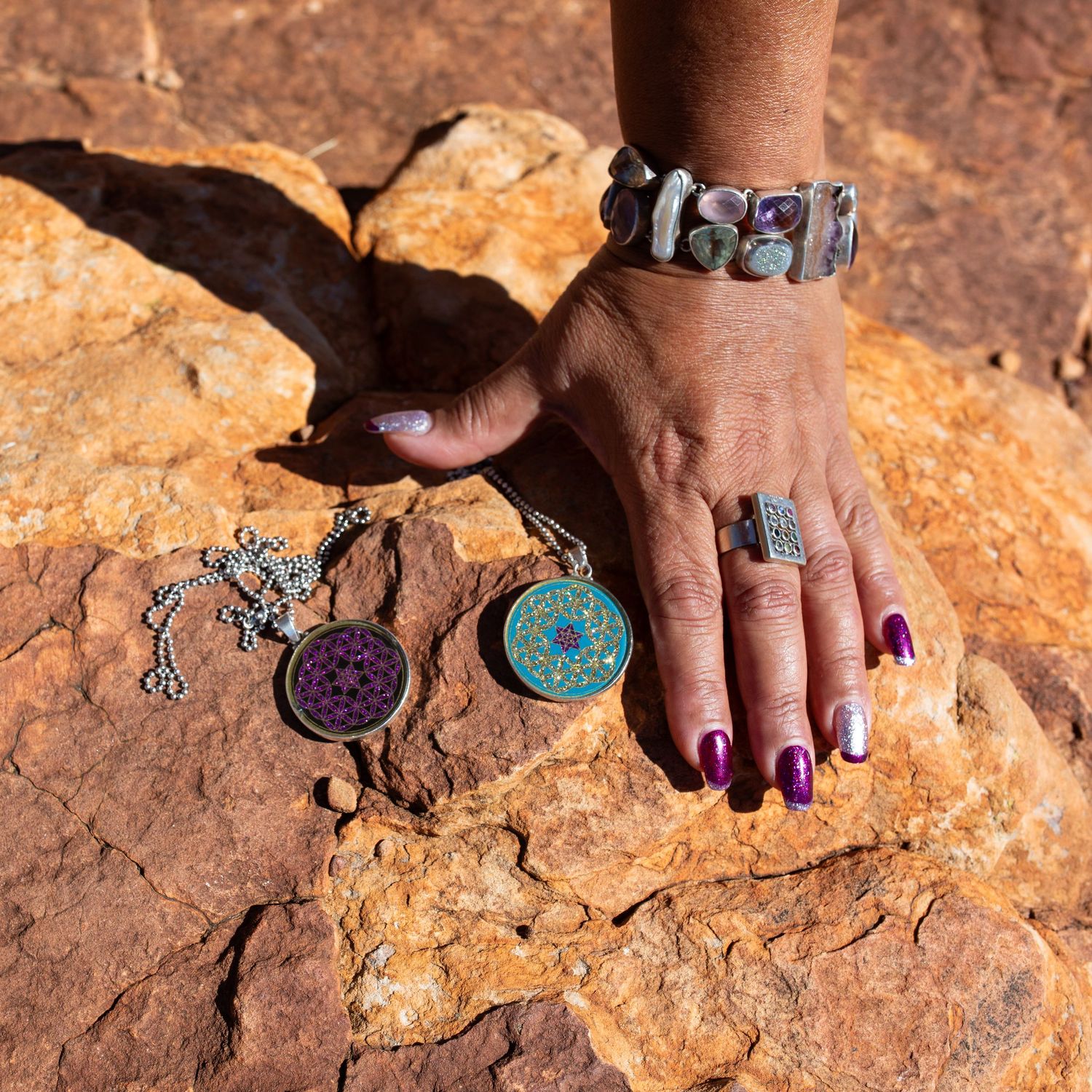 Hands delicately arranging handmade turquoise jewelry pieces on textured orange sandstone rock surface.