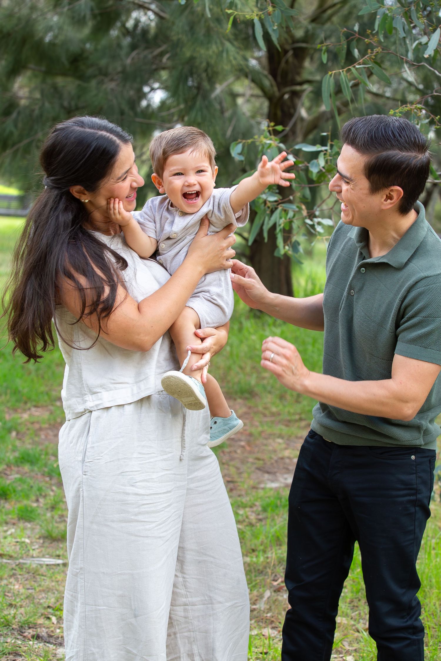 Happy young family with laughing toddler enjoying a sunny day outdoors in a lush green park setting.