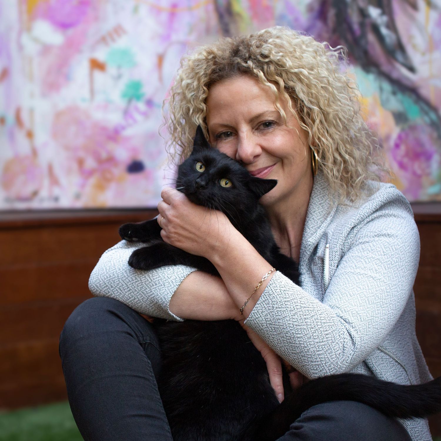 An adorable black cat being cuddled against a colorful wall background.
