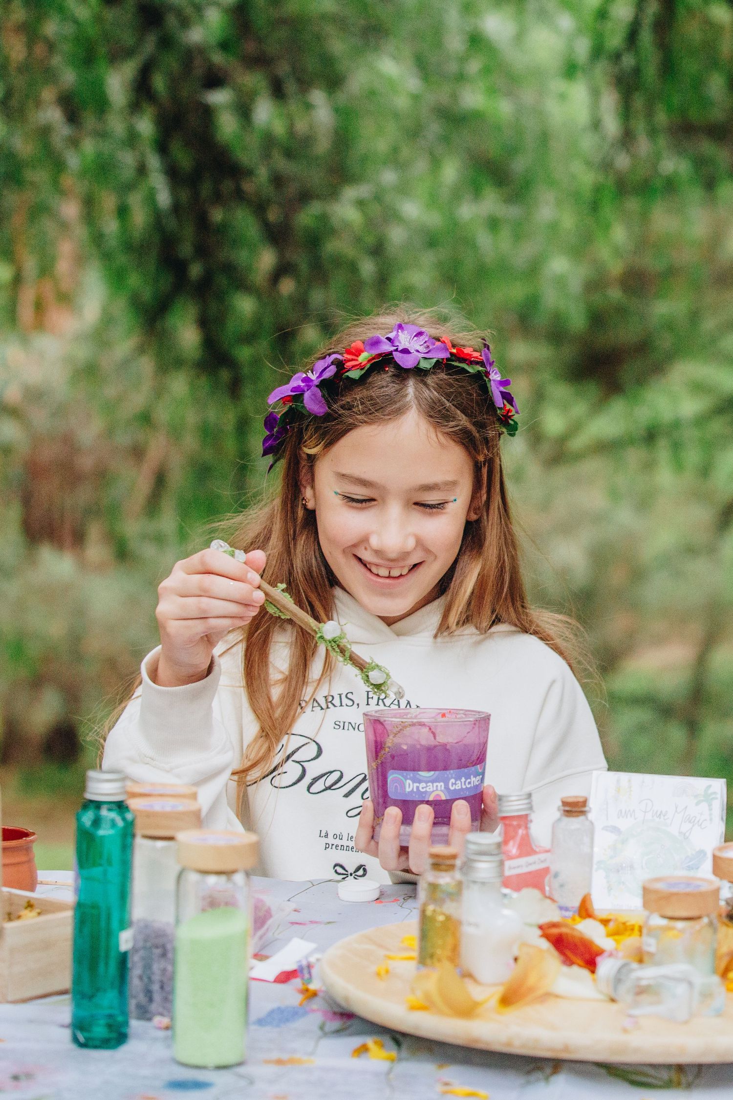 Happy girl with flower crown adding ingredient to purple potion jar outdoors.