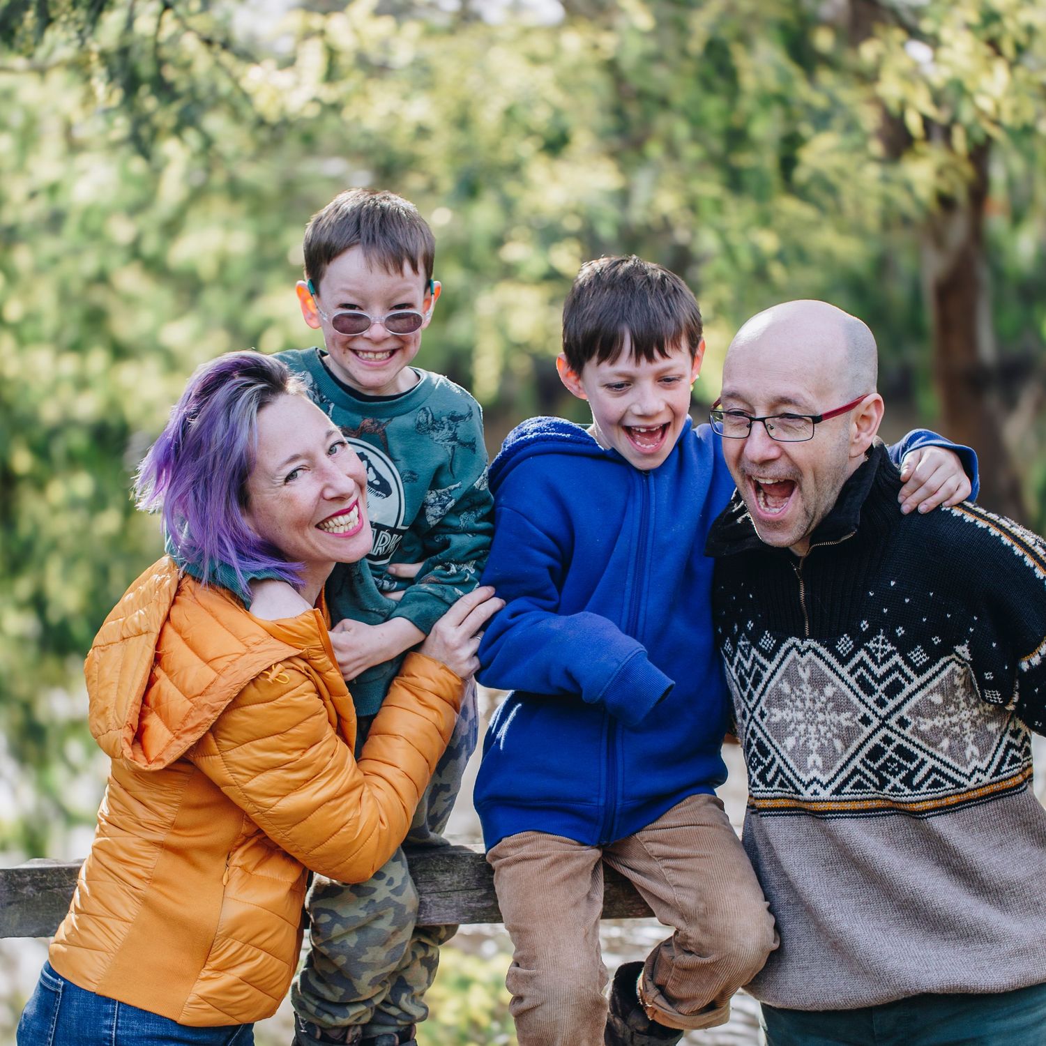 A joyful family enjoys playful moments together outdoors in casual attire against a natural green background.