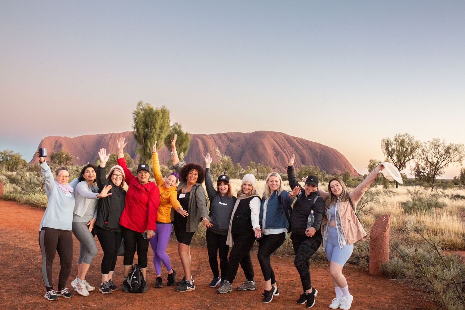 Group of tourists admiring the majestic Uluru rock formation at sunset in the Australian outback.