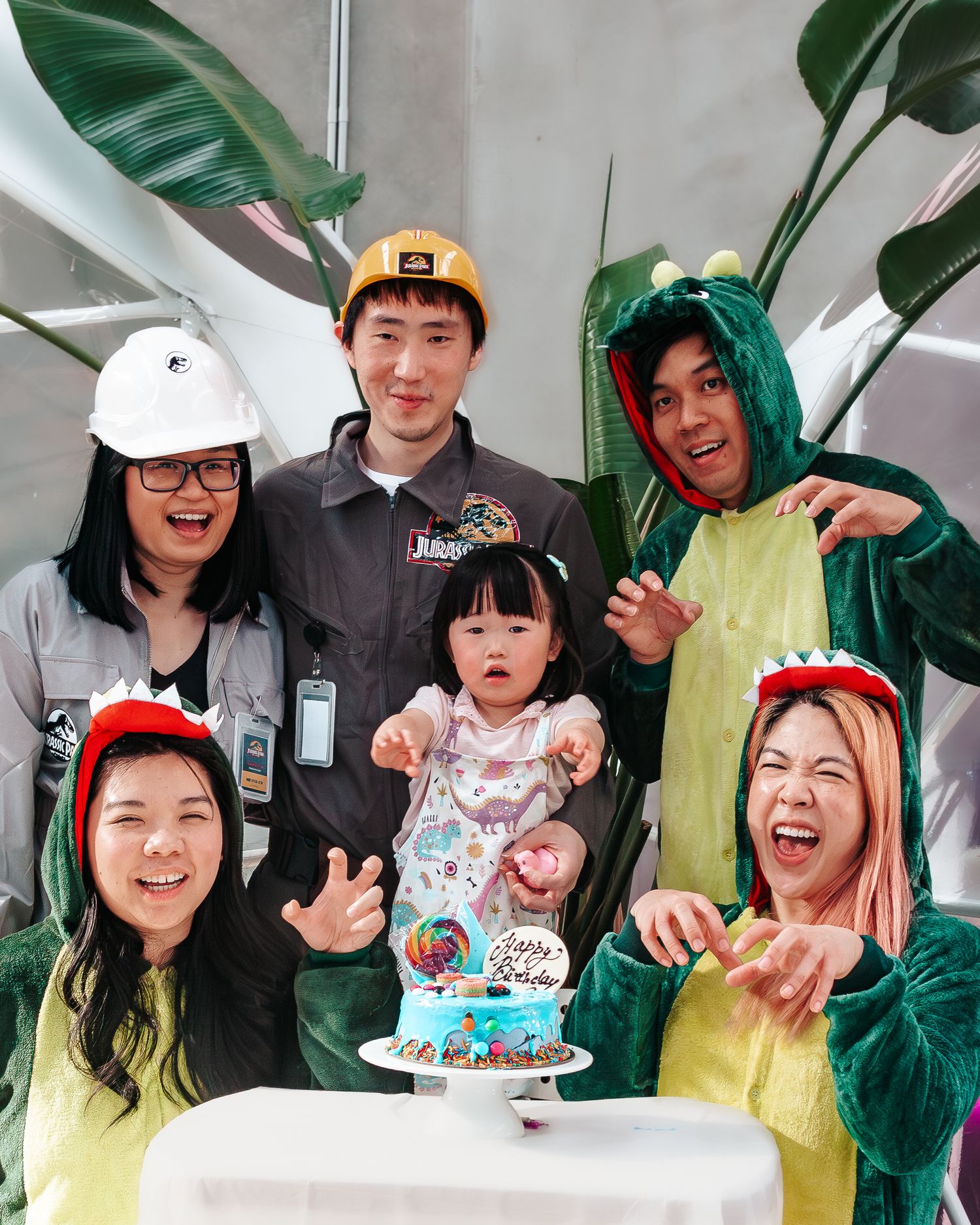 A group celebrating a birthday with cake while wearing fun costumes and making peace signs.