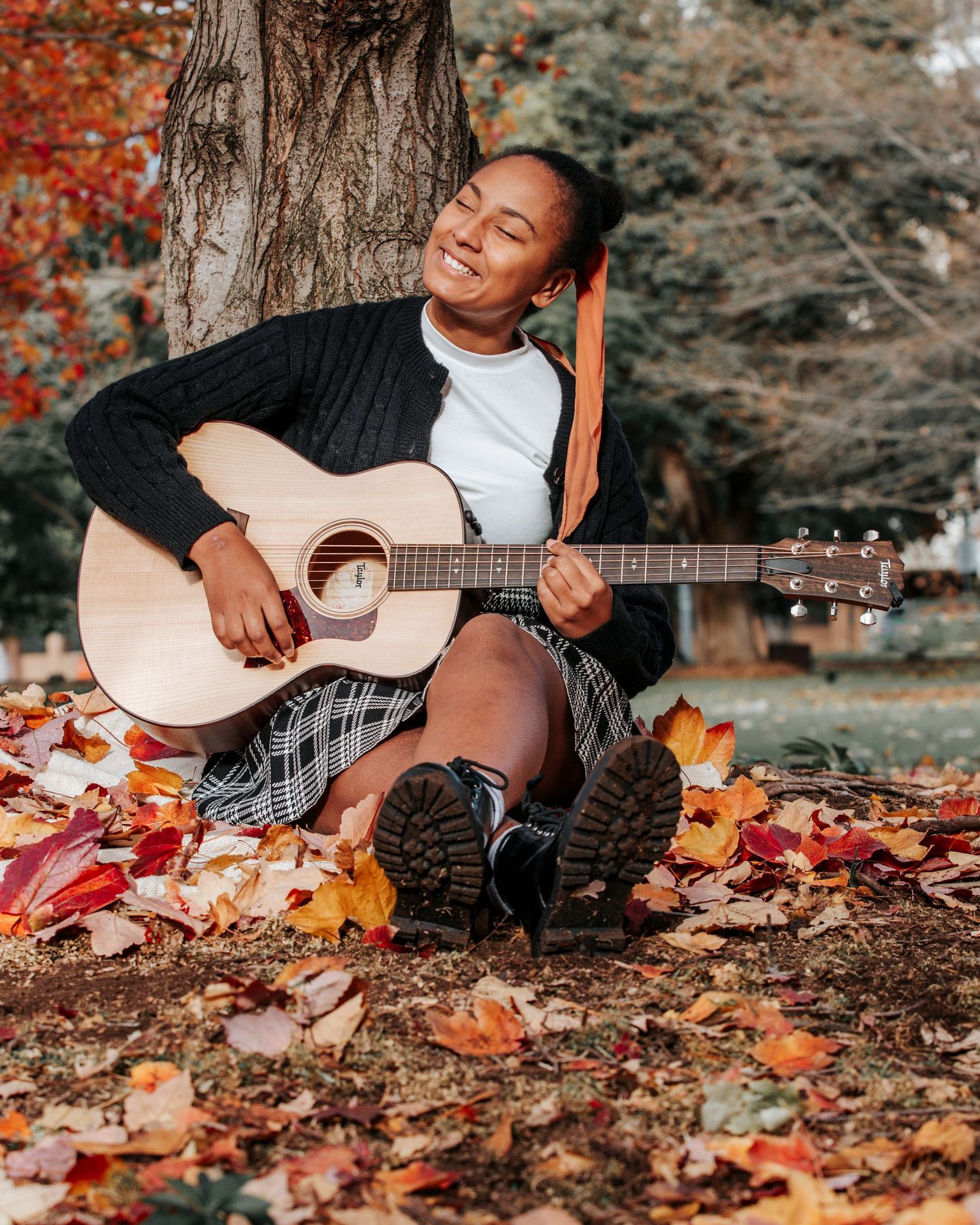 Musician playing acoustic guitar while sitting on autumn leaves in the woods.