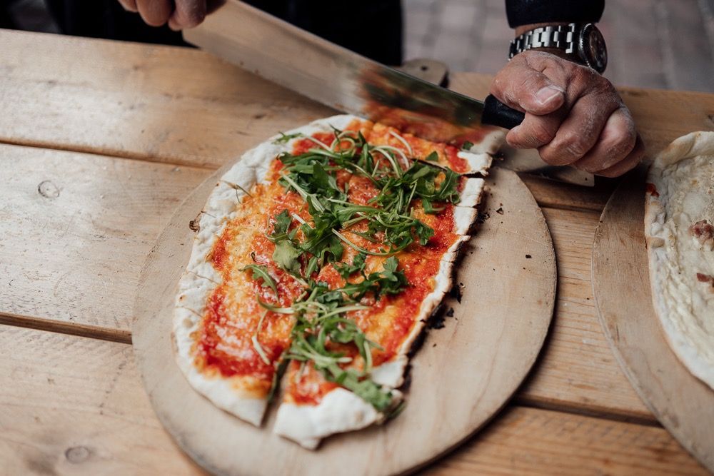 Hands preparing a rustic pizza on a wooden surface with fresh herbs and toppings.
