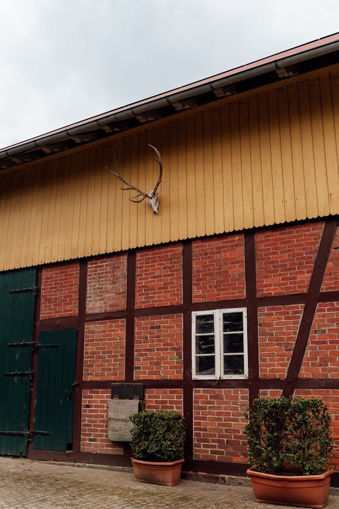 Exterior view of a brick stable building with green shutters and tan upper siding along a continuous wall.