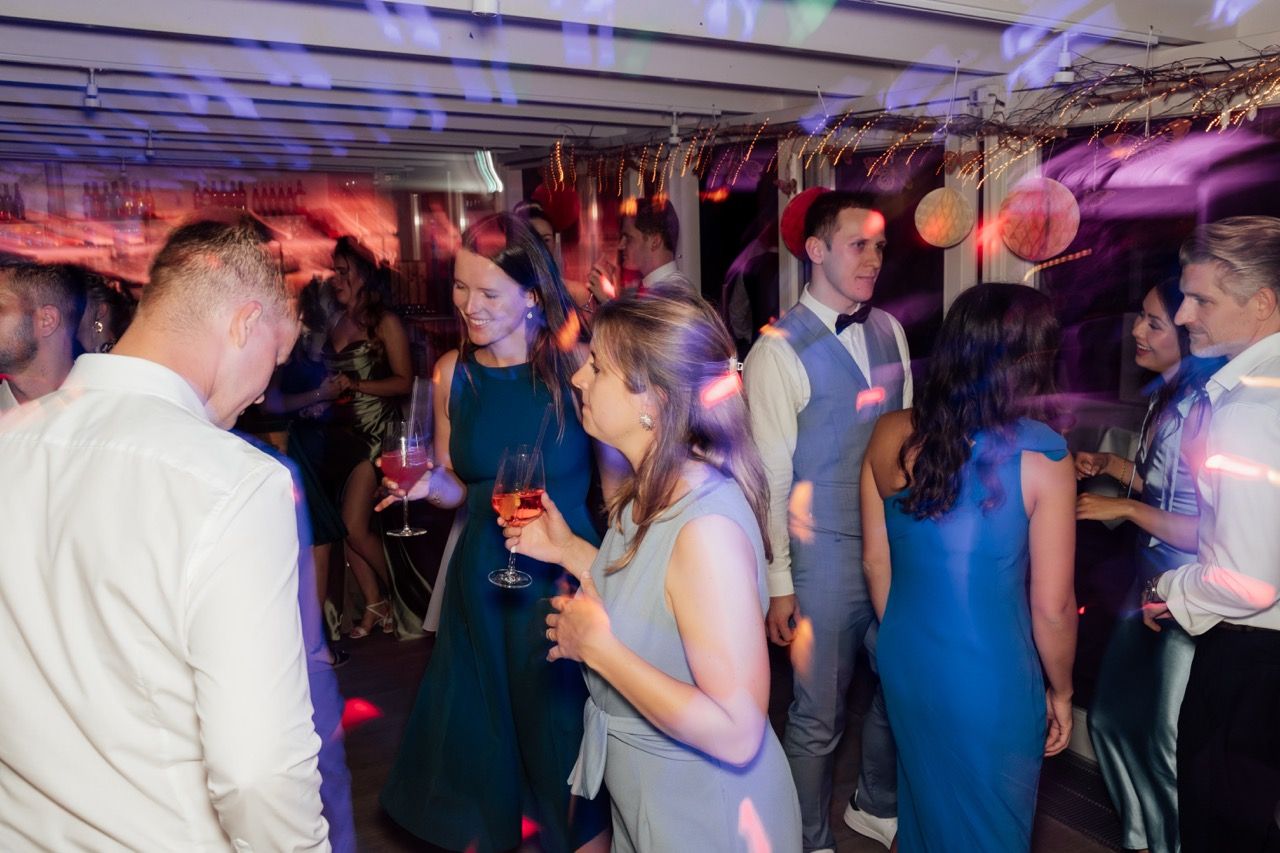Guests mingling and dancing at a lively indoor party with colorful pink and blue lighting.