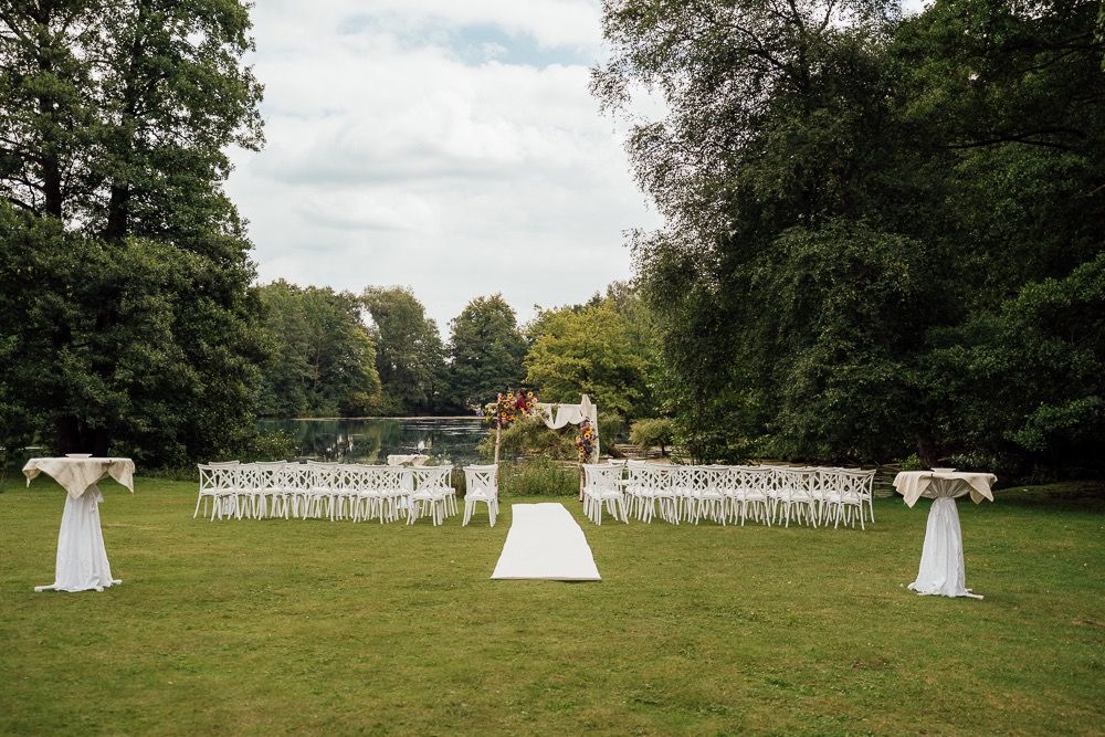 White chairs arranged in rows for an outdoor wedding ceremony with decorative pillars on a green lawn surrounded by trees.
