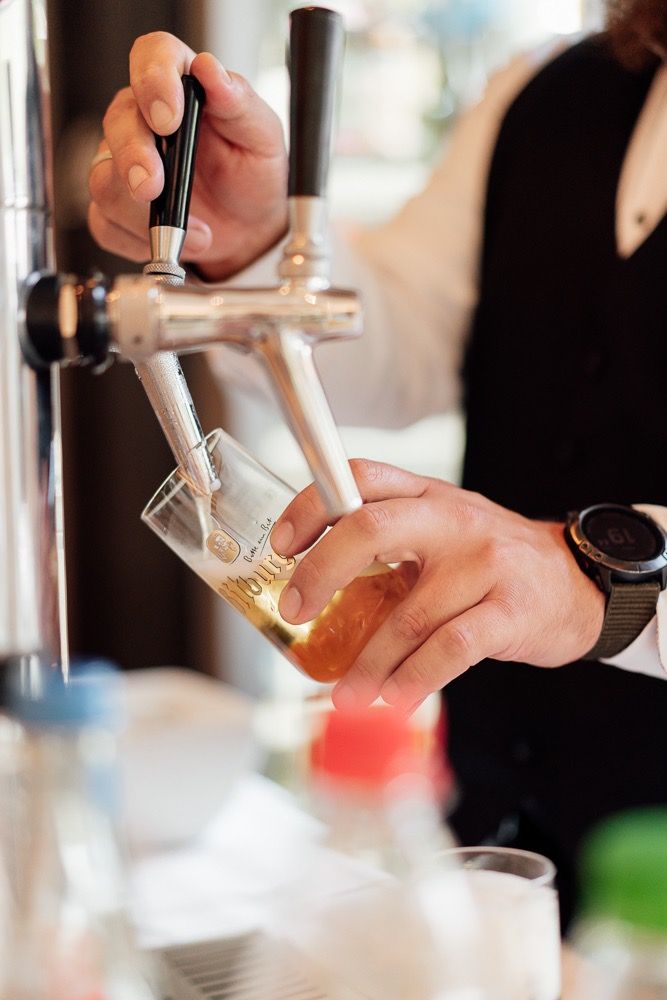 Bartender pouring draft beer from tap into glass at bar counter showing foamy head formation.