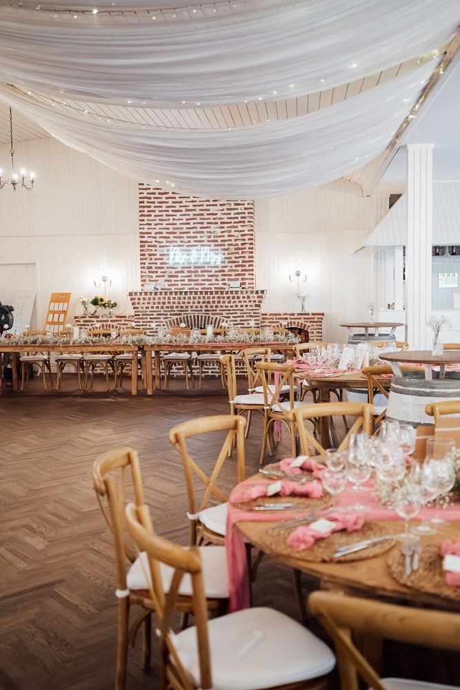 Wedding venue with draped white fabric ceiling, exposed brick walls, and farmhouse tables arranged for a reception.