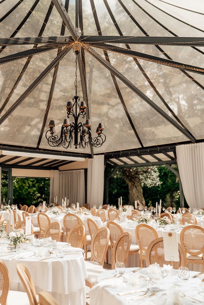 Elegant outdoor wedding reception setup with white canopy tents, chandeliers, and round tables with cream-colored chair covers.