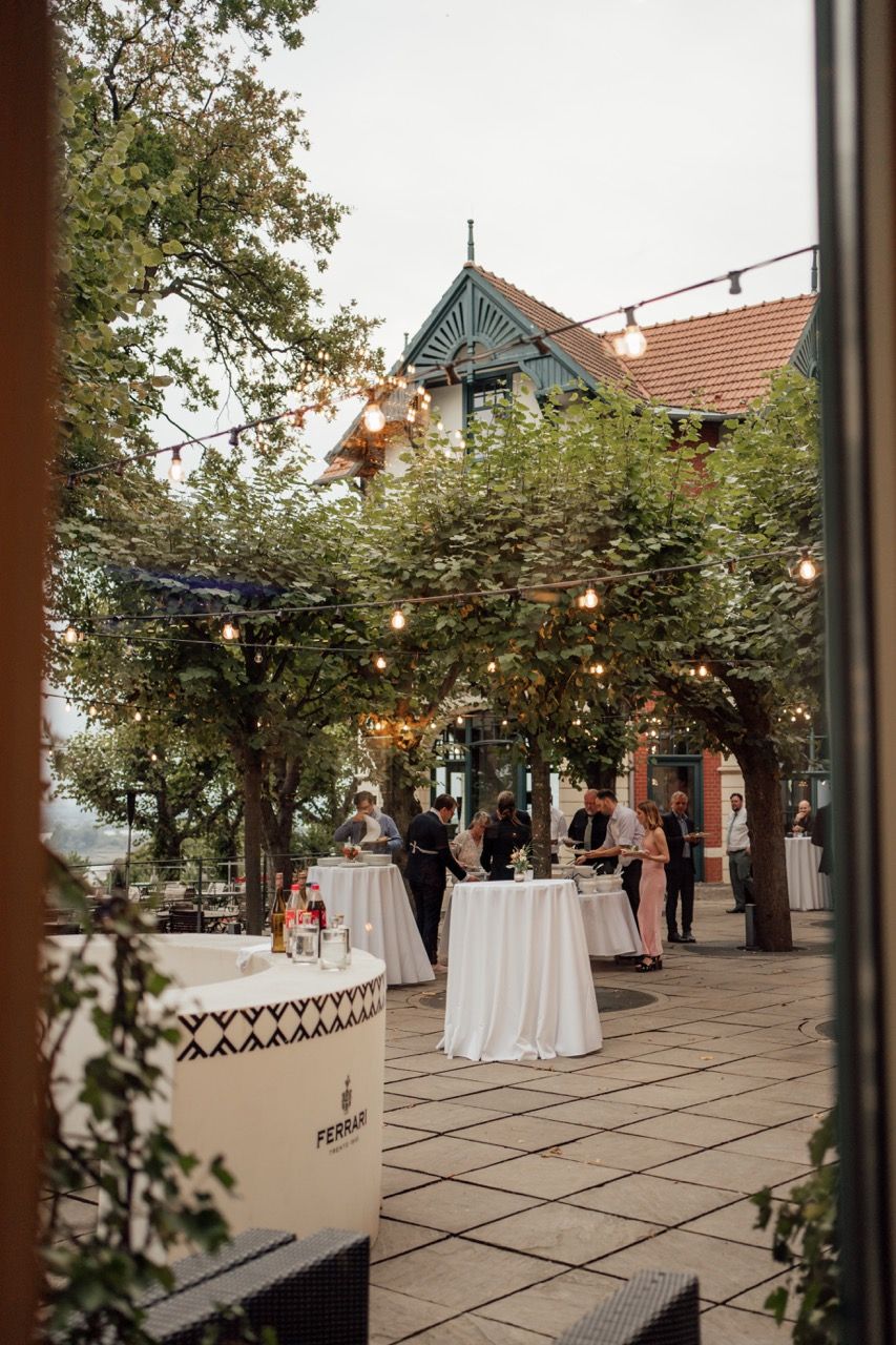 Guests mingle at an elegant outdoor wedding cocktail hour with string lights and Ferrari Trento branded bar station.