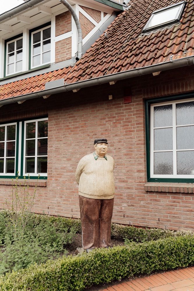 A decorative garden statue stands in front of a brick house with green-trimmed windows and a tiled roof.
