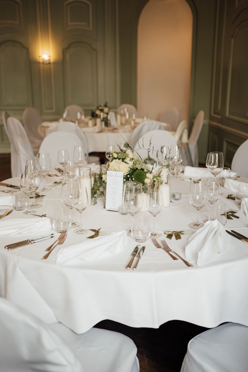 Elegant wedding reception table with white linen, crystal glasses, gold cutlery, and floral centerpiece in a classic venue.
